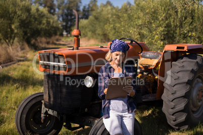 Woman leaning on tractor while writing on clipboard