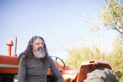 Thoughtful man sitting against tractor in olive farm