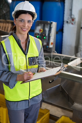 Portrait of female technician writing in clipboard