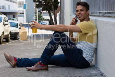 Smiling young man talking on smart phone while sitting on sidewalk