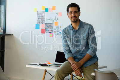 Portrait of smiling man sitting on desk at office