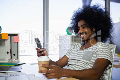 Smiling man using phone while having coffee in office