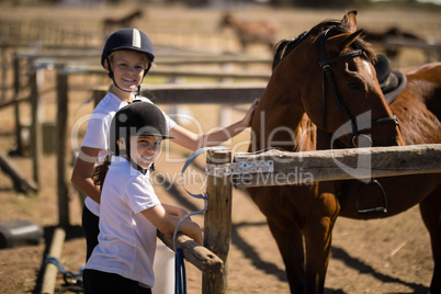 Smiling girls standing near the brown horse in the ranch