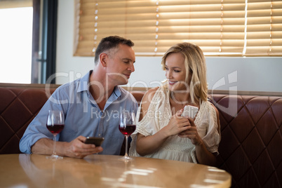 Couple using mobile phones while having glass of wine
