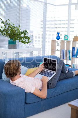 Male executive using laptop while relaxing on sofa