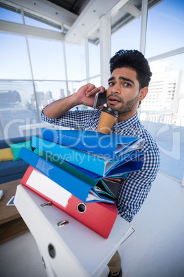 Male executive holding stack of files while talking on mobile phone