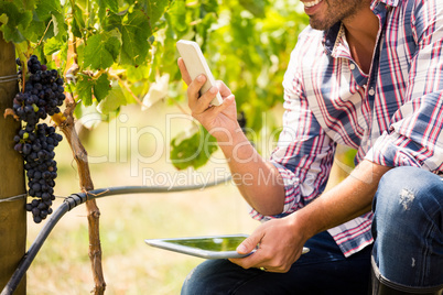 Midsection of man using phone while holding tablet