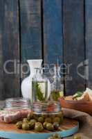 Olives in container by herbs with oil bottle on table