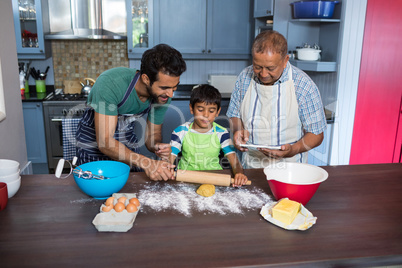 Father assisting son for preparing food while standing by man using tablet