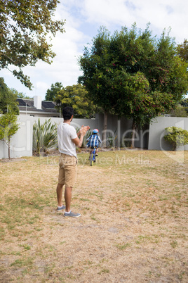 Father applauding while son cycling in yard