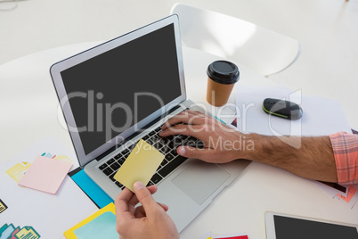 Cropped hands of designer holding adhesive note while using laptop