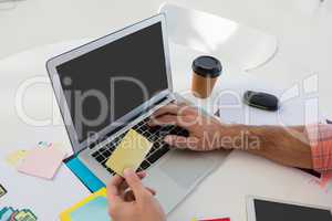 Cropped hands of designer holding adhesive note while using laptop