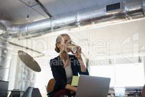 Businesswoman having drink while sitting with laptop