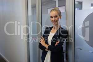 Smiling businesswoman with arms crossed standing by door at office