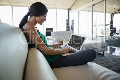 Side view of woman using laptop on sofa at office