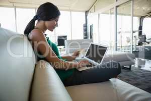 Side view of woman using laptop on sofa at office