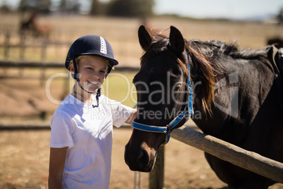 Smiling girl standing near the brown horse in the ranch