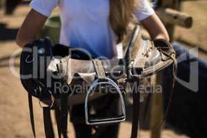 Girl holding horse saddle in the ranch