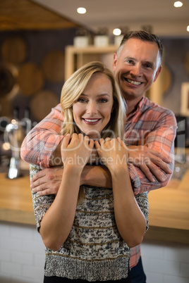 Smiling man embracing woman from back in bar