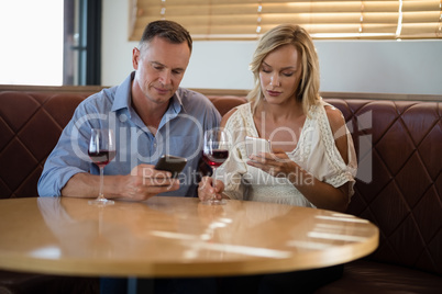 Couple using mobile phones while having glass of wine