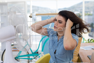 Female executive enjoying breeze from table fan