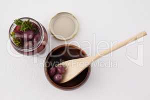 High angle view of red olives in jar and container with wooden spoon