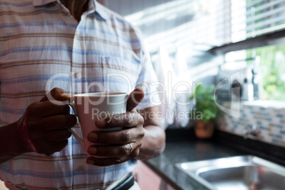 Midsection of man holding coffee cup by window