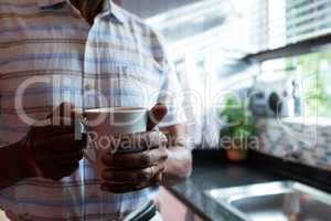 Midsection of man holding coffee cup by window