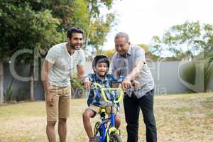 Father and grandfather assisting boy for riding bicycle
