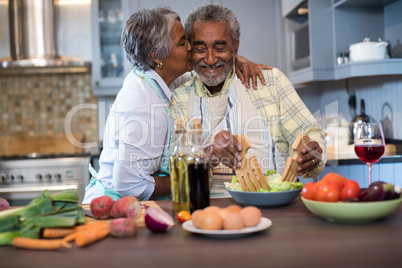 Senior woman kissing man while preparing food