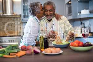 Senior woman kissing man while preparing food