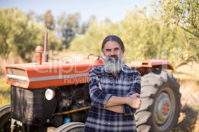 Portrait of happy man standing with arms crossed against tractor