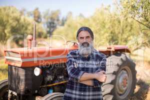 Portrait of happy man standing with arms crossed against tractor