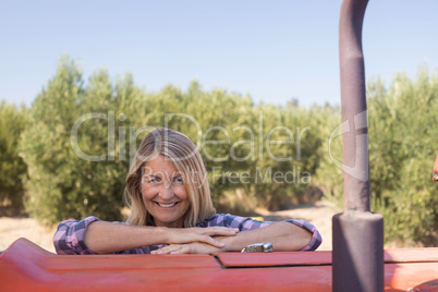 Portrait of happy woman leaning on tractor in olive farm