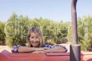 Portrait of happy woman leaning on tractor in olive farm