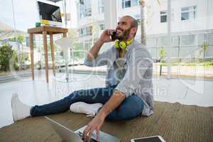 Cheerful designer talking on mobile phone while sitting on floor