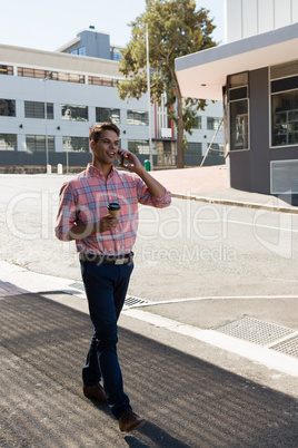 Young man having drink while talking on mobile phone