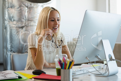 Woman holding eyeglasses at desk in office