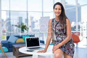 Female executive sitting on desk in the office