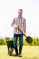 Portrait of young man holding shovel by wheelbarrow