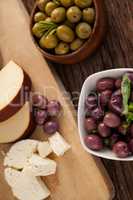 Brown and green olives by vegetable and cheese on cutting board
