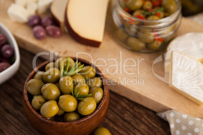 Green olives in container by cheese and vegetable