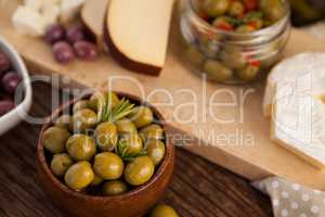 Green olives in container by cheese and vegetable