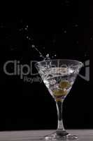 Vodka splashing in martini glass with olives