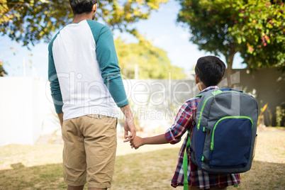 Rear view of father holding hand of son with backpack