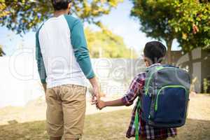 Rear view of father holding hand of son with backpack