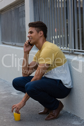 Young man talking on smart phone while crocuhing by wall