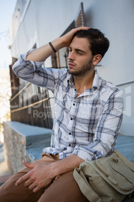 Man with eyes closed sitting on retaining wall