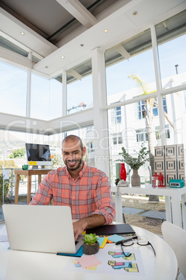 Smiling designer using laptop while sitting at desk