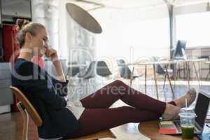 Businesswoman talking on smart phone while relaxing on chair at office